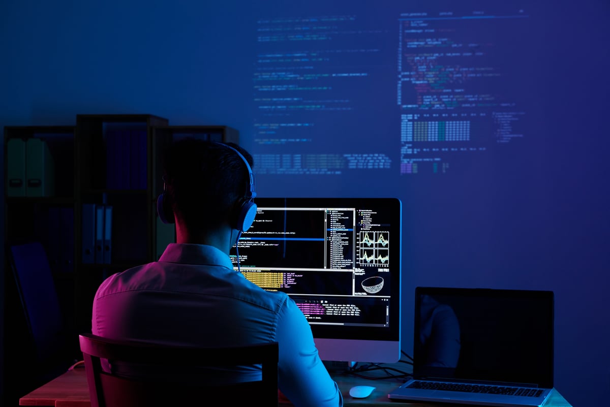 A person working at computer screens in a dark room