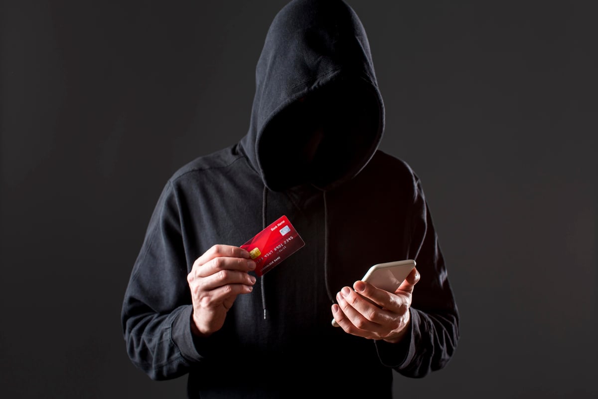A person in a hood holding a credit card and phone